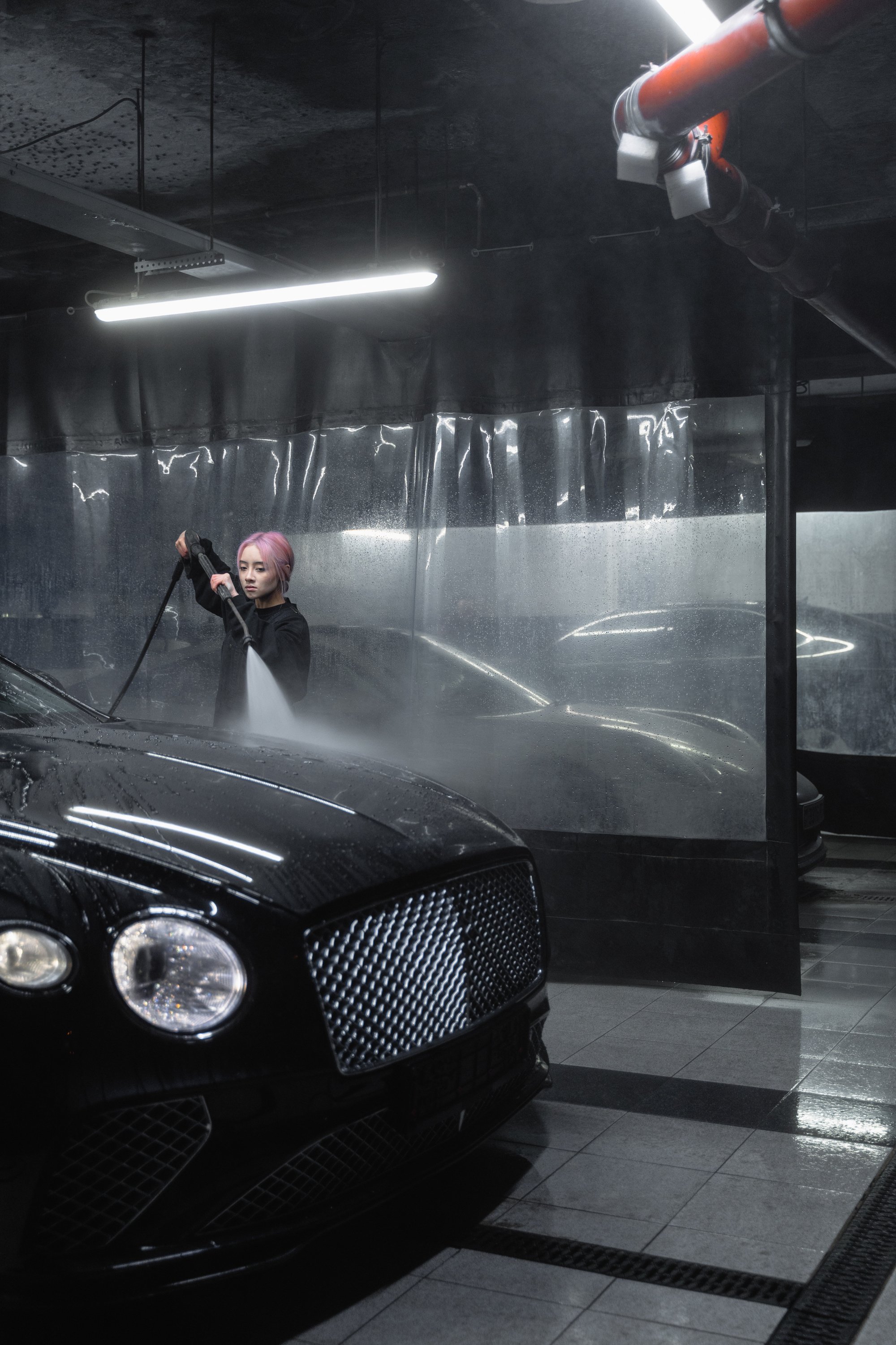 Woman Cleaning the Black Car Using a Washer Pressure Hose